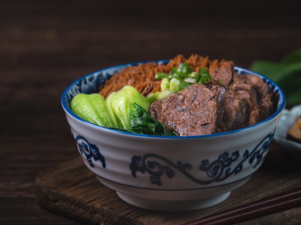 A bowl of Taiwanese beef noodle soup with braised beef shank, noodles, greens and spring onion
