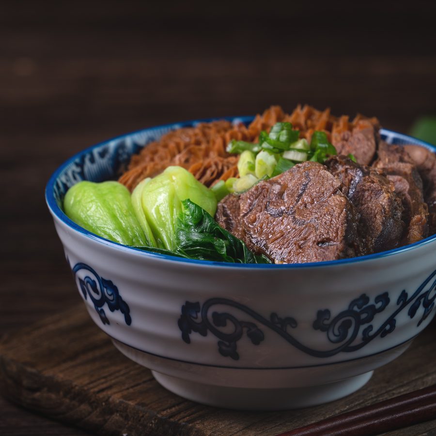 A bowl of Taiwanese beef noodle soup with braised beef shank, noodles and greens