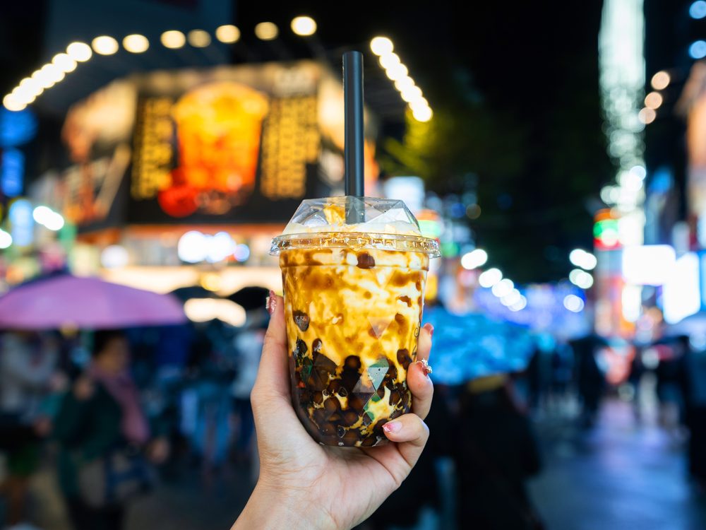 A hand holding a cup of brown sugar bubble tea with tapioca pearls against the neon lights of Ximending in Taipei