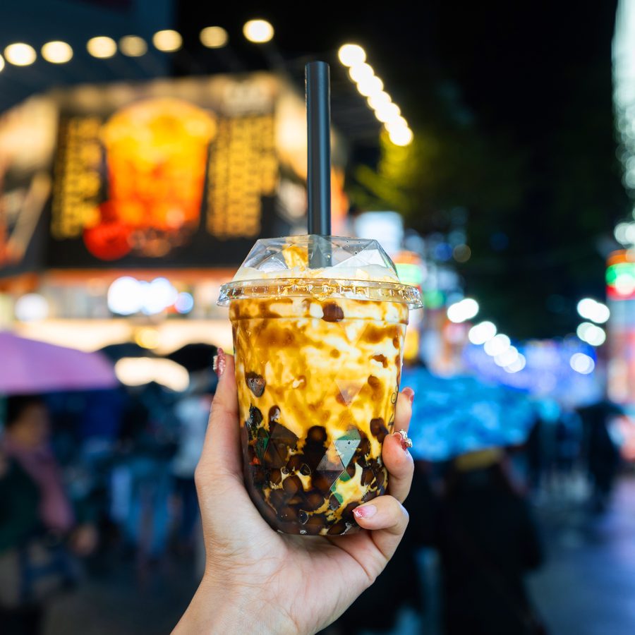 A cup of brown sugar bubble tea held up against the neon lights of Ximending at night