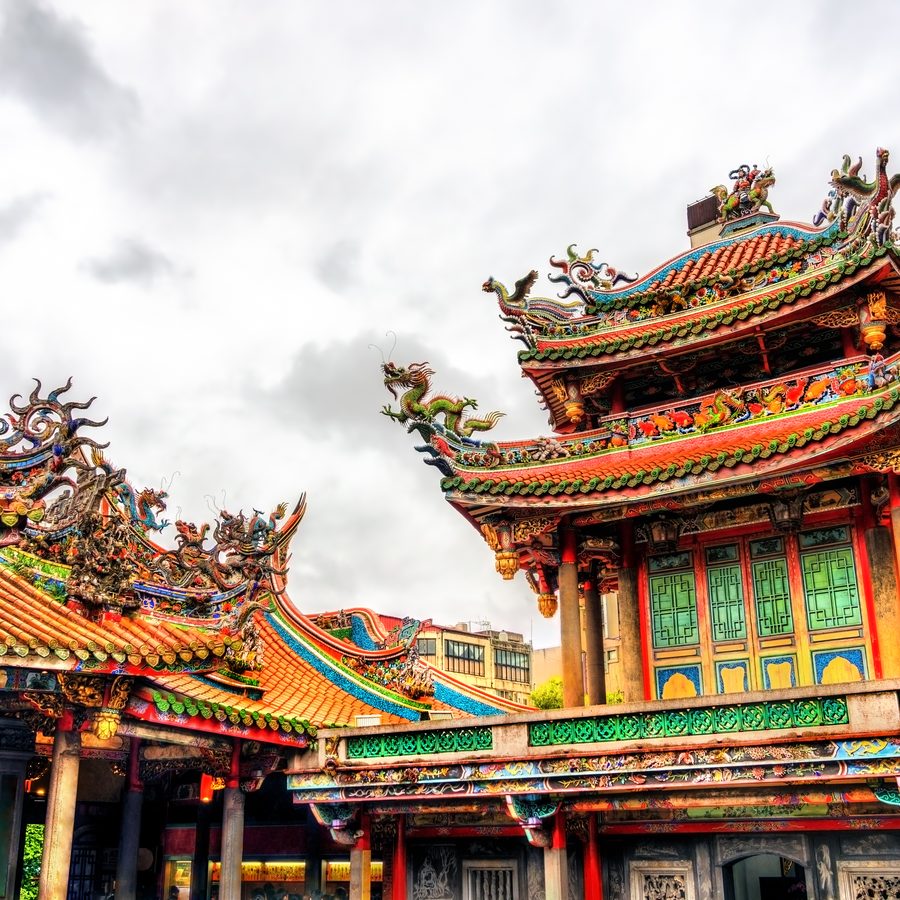The ornate carved and painted roofs of Longshan Temple in Taipei against a cloudy sky